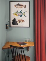 A framed fish illustration on a wall, a desk with a chair, a lamp, and two glasses on the desk.