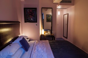 Hotellihuone, jossa on sänky, työpöytä tuolilla, peili ja taideteoksia seinillä.