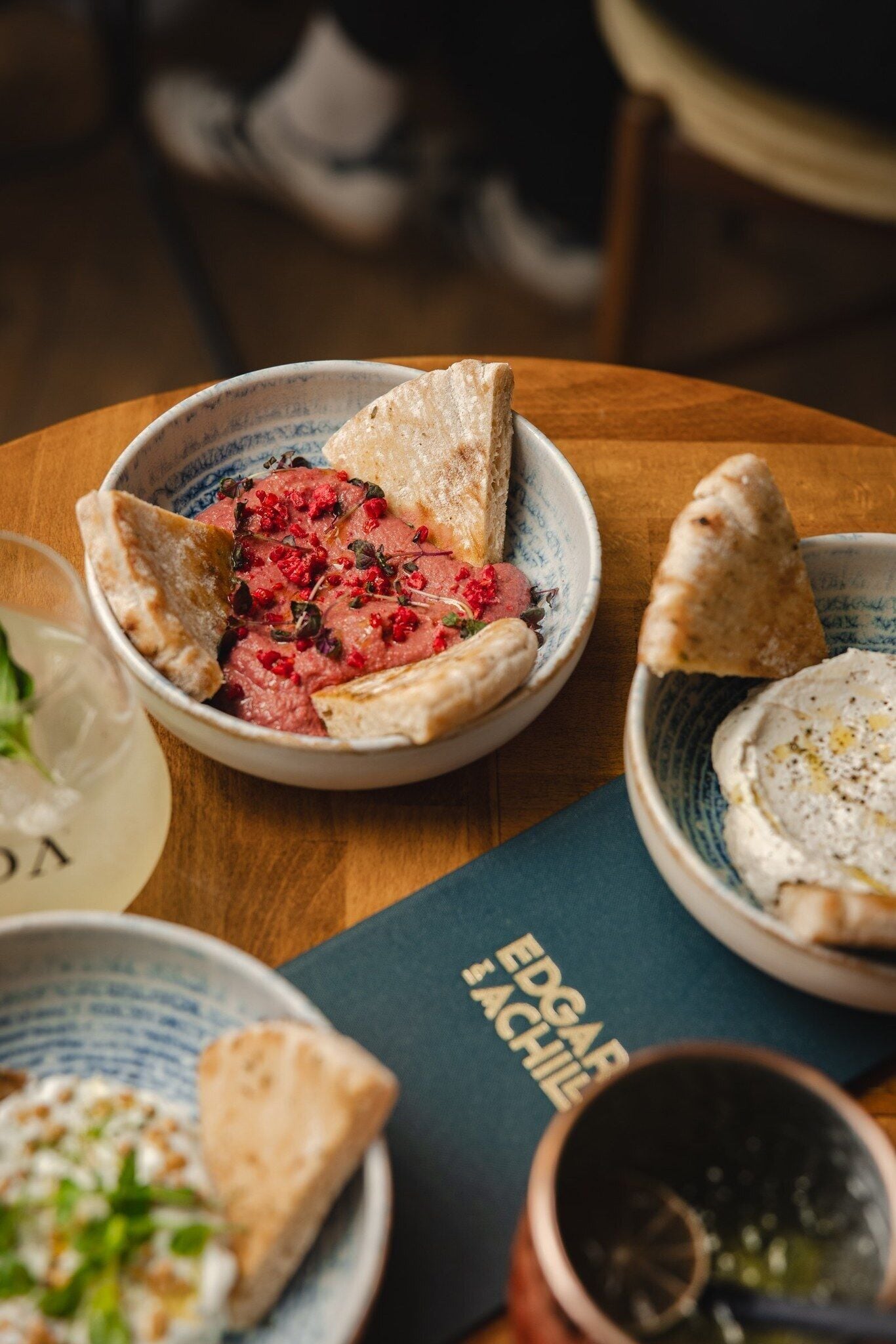 Una mesa con varios platos, incluyendo un tazón de carne, un tazón de hummus y una taza de té.