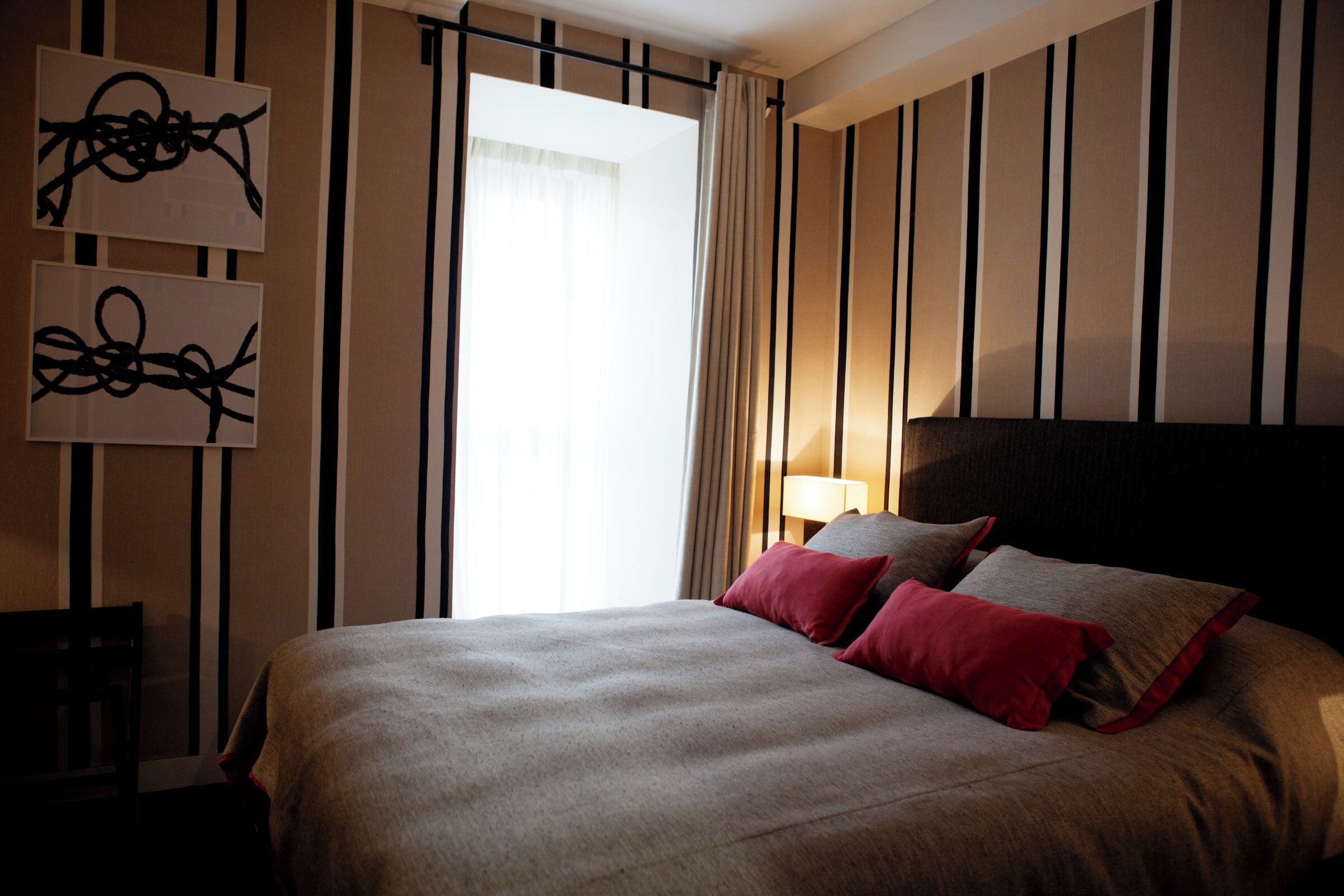 Habitación de hotel con una cama grande, dos almohadas, una mesita de noche y una pared con rayas verticales y arte abstracto.