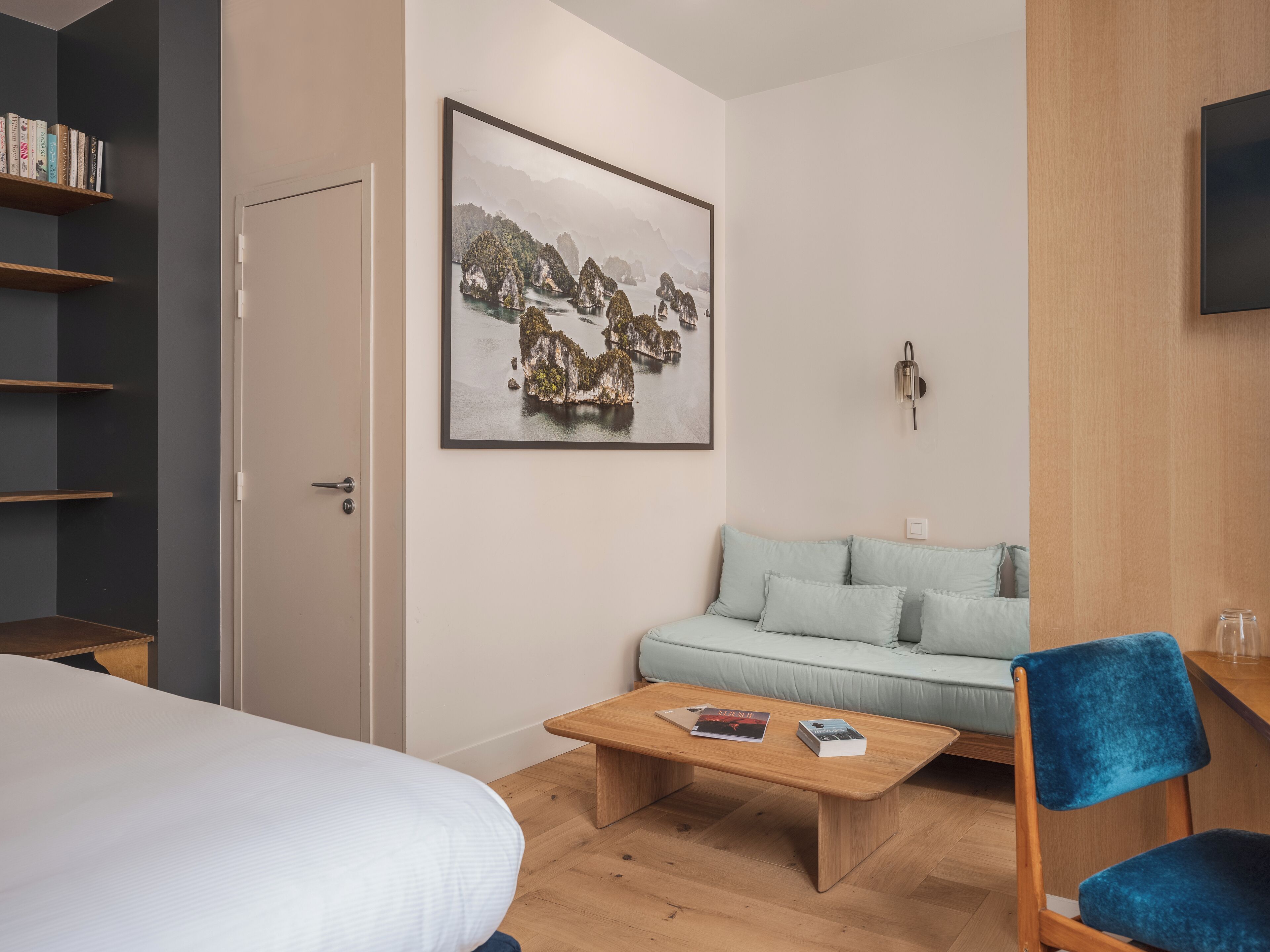 Ein modernes Zimmer mit einem Bett, einem Holztischchen, einem hellblauen Sofa und einem Bücherregal.