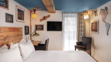 Habitación de hotel con cabecera de madera, cama con ropa blanca, escritorio con silla, televisión y obras de arte en las paredes.