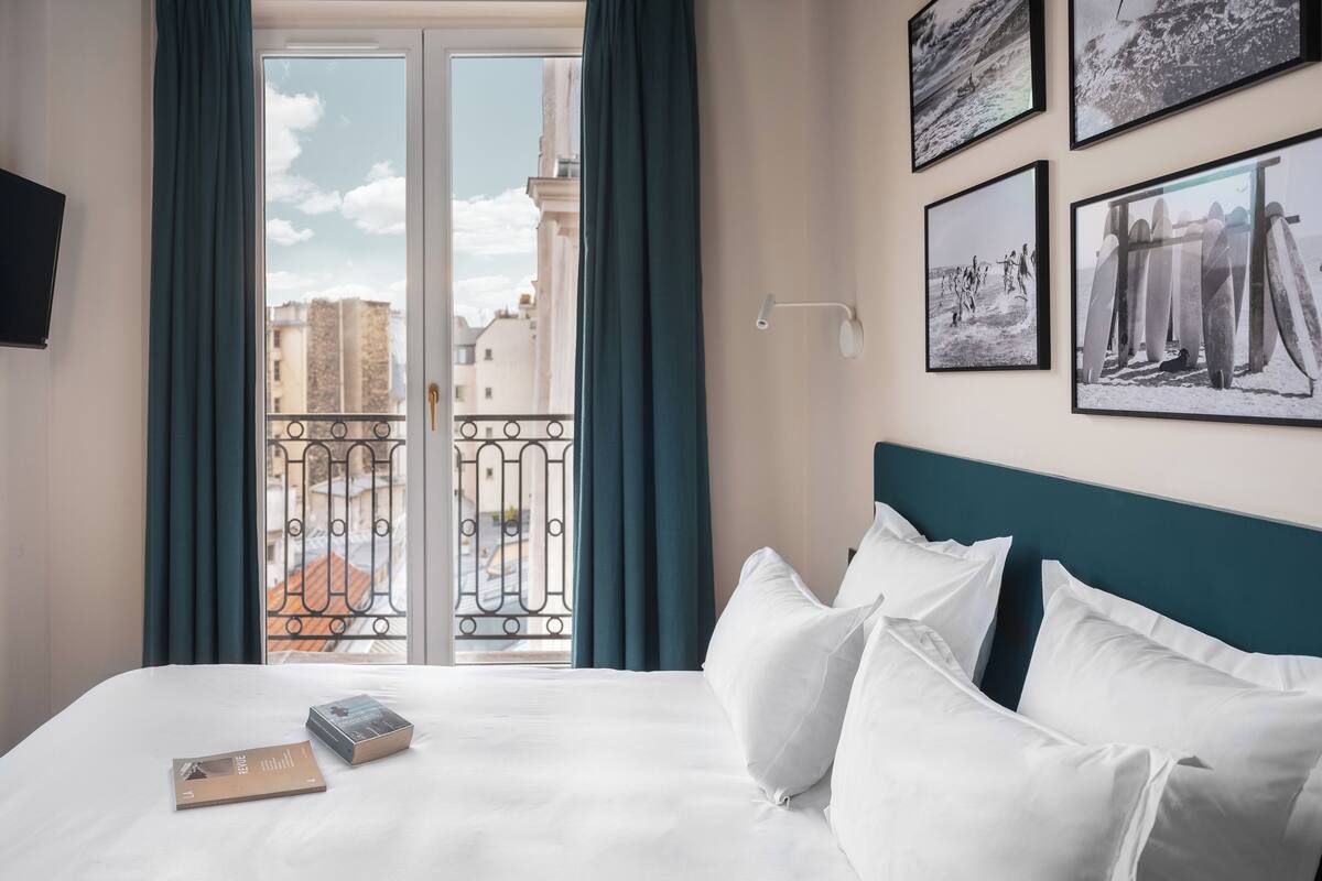 A hotel room with a bed, a window with curtains, and several framed pictures on the wall.