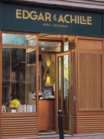 The exterior of Edgar & Achille Hotel & Restaurant with a wooden facade and large glass doors.