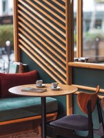 Ein gemütliches Café mit einem runden Tisch, zwei Tassen, einem Buch und einem Paravent aus Holzlatten.