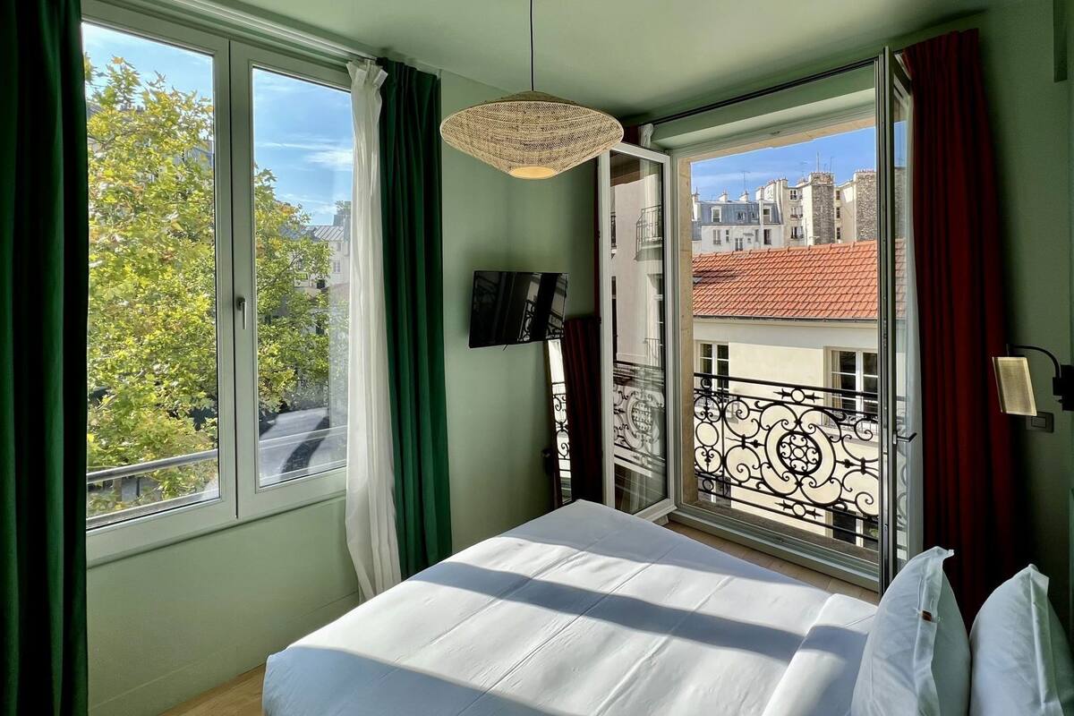 A bedroom with a bed, a TV, a window with curtains, and a balcony with a railing.