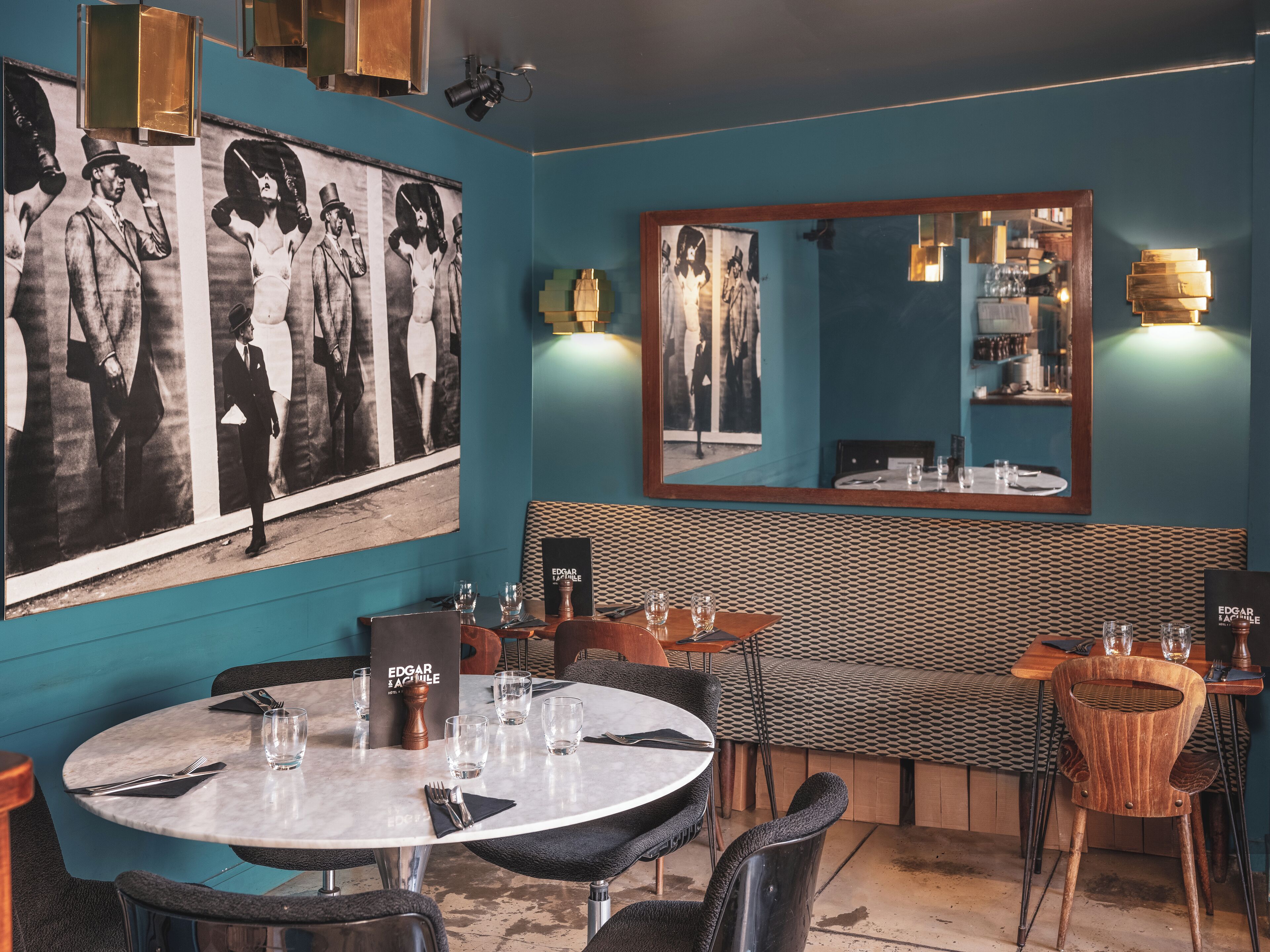 A restaurant with a teal wall, black and white photographs, a wooden bench, and a round table with chairs.