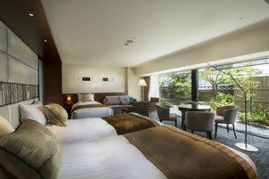 Habitación de hotel con dos camas, una zona de estar con mesa y sillas, y vista al exterior.