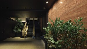 Un pasillo interior moderno con una escalera, plantas en macetas y una pared de mármol.