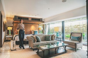 A modern hotel room with a sofa, armchair, and glass coffee table.