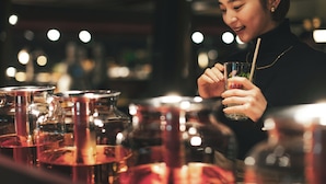 Una persona sosteniendo un vaso con pajita, de pie frente a una barra con diferentes botellas y recipientes.