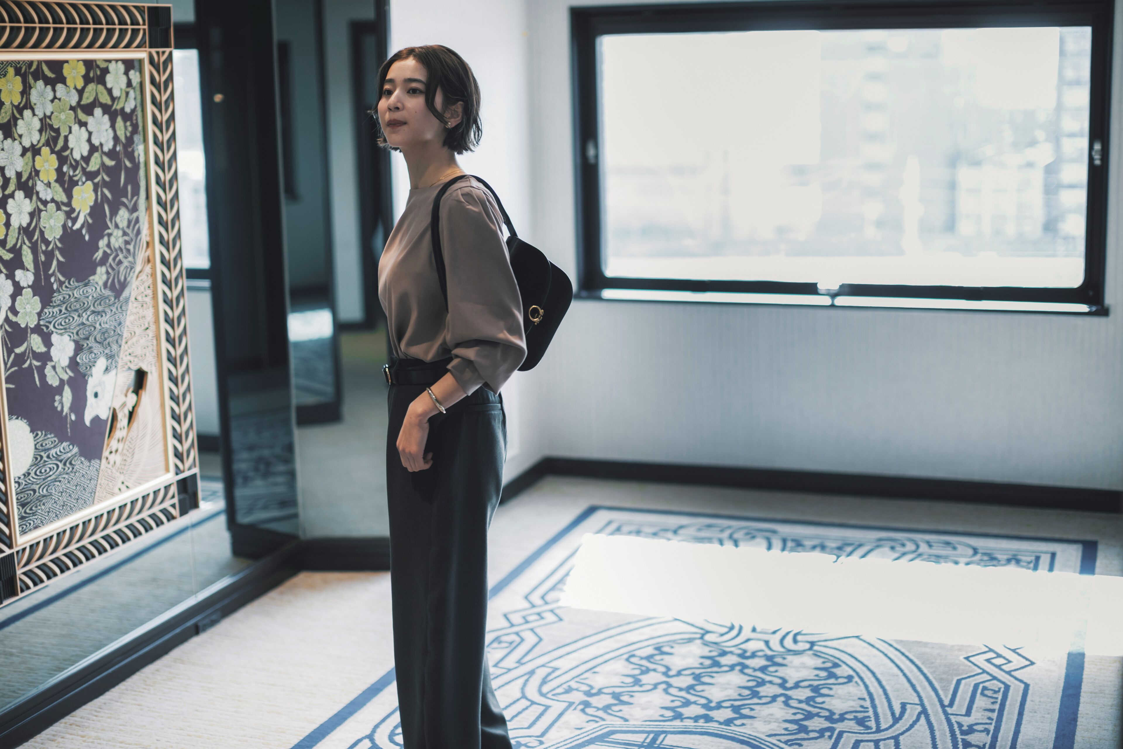 A person standing in a hallway with a large window and a patterned floor.