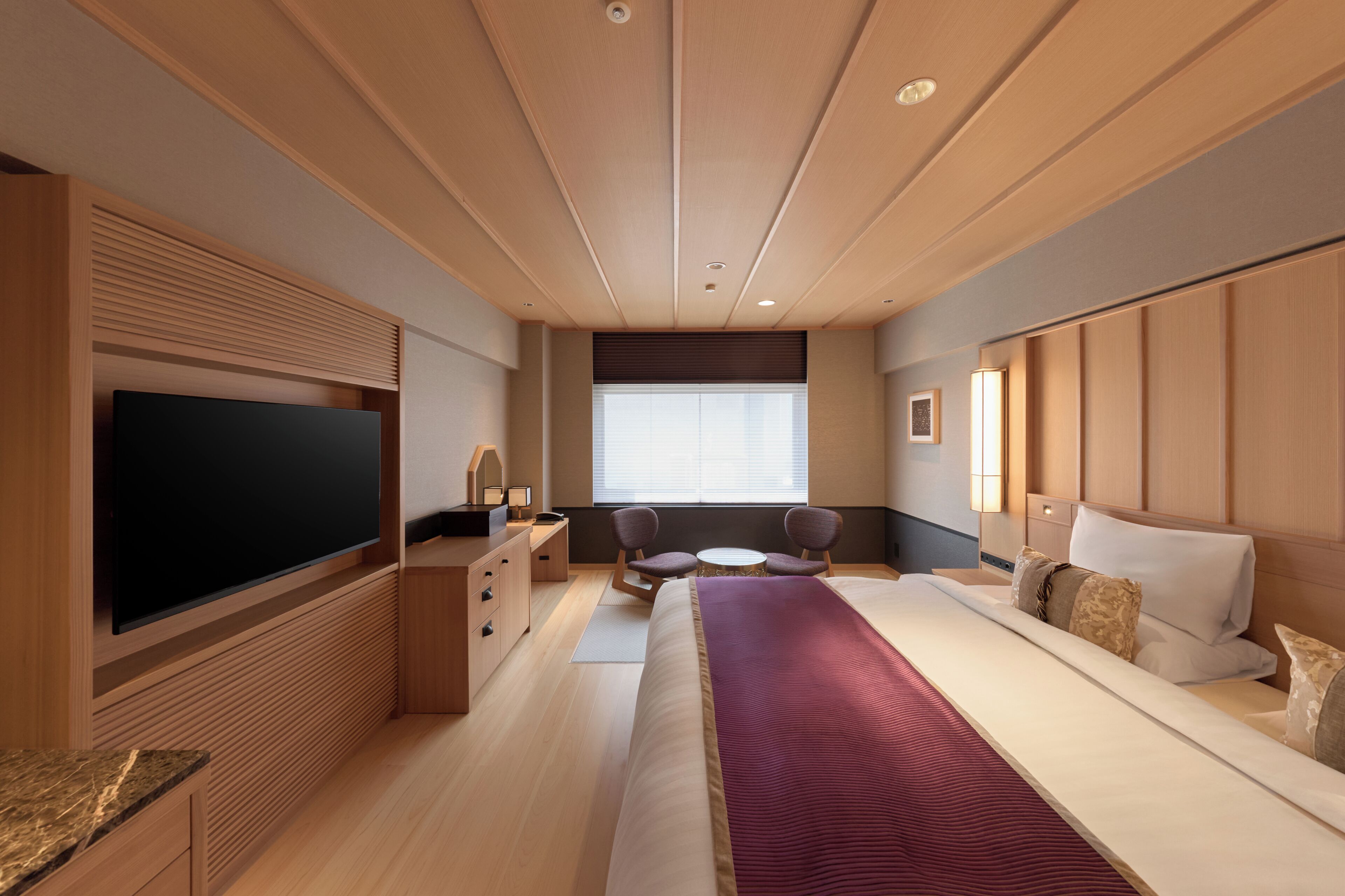 A modern hotel room with a large bed, a flat-screen TV, a desk with a chair, and a window with blinds.