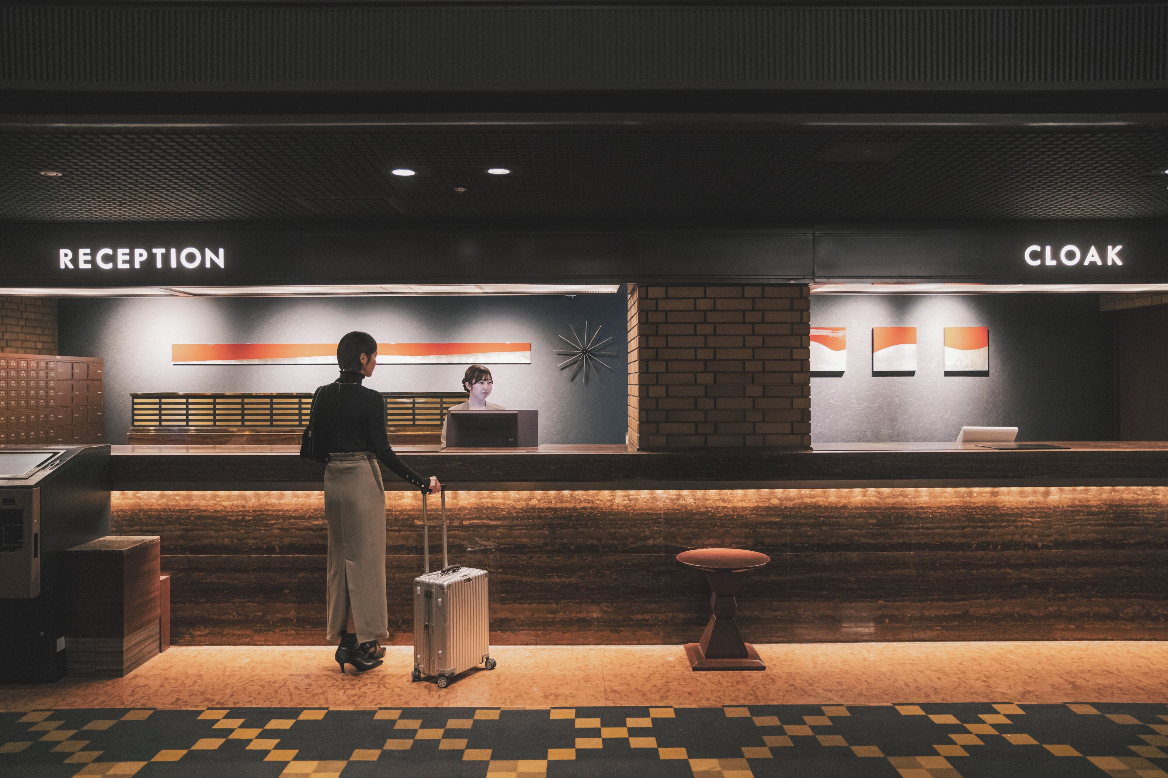 A reception area with a reception desk, a cloakroom, and a person with a suitcase.