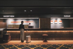Ein Empfangsbereich mit einer Rezeption, einer Garderobe und einer Person mit einem Koffer.