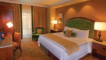 Una habitación de hotel con una cama grande, un sillón verde, un escritorio con lámpara y una mesita de noche con lámpara.