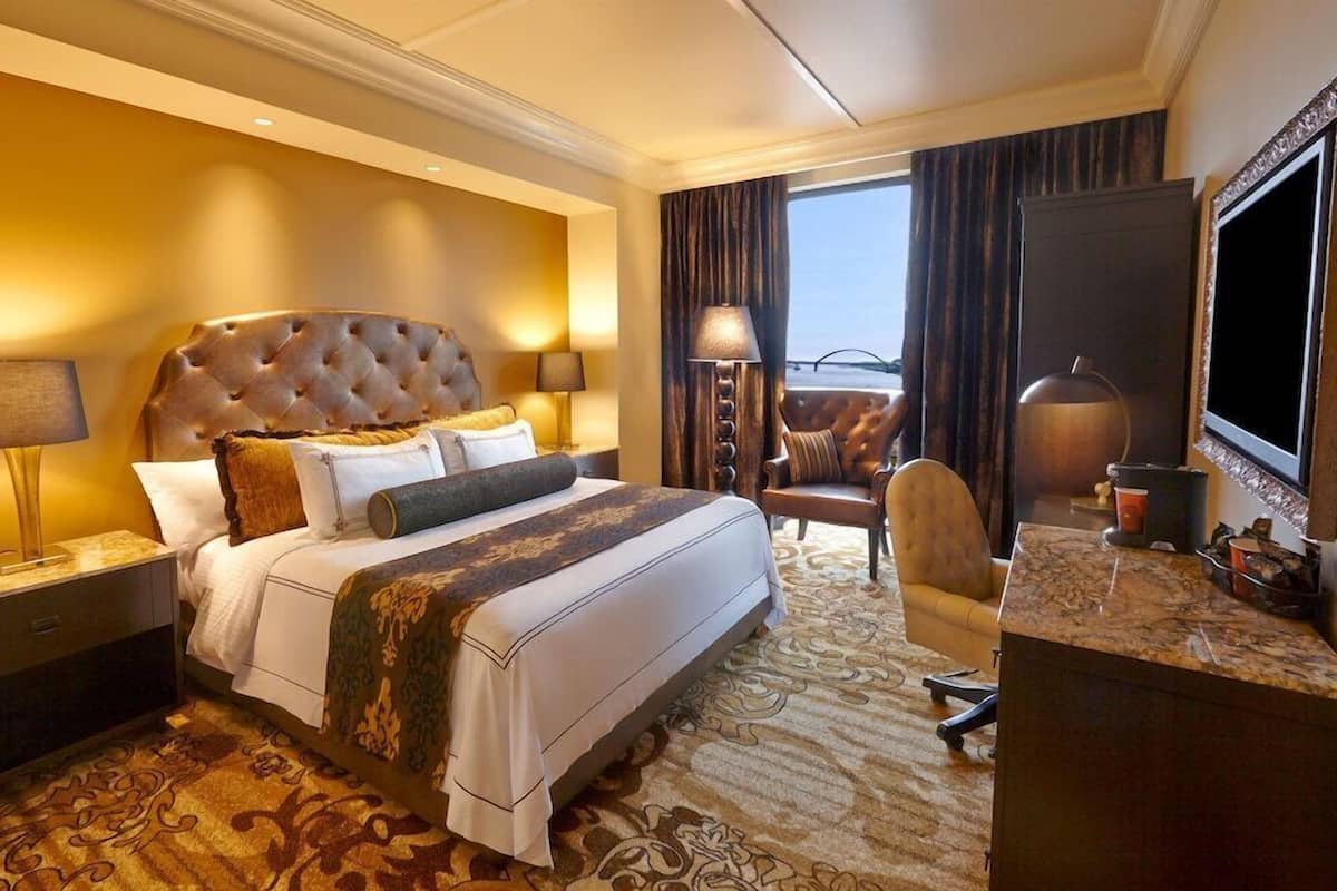 A hotel room with a large bed, a desk with a television, and a view of the sea.