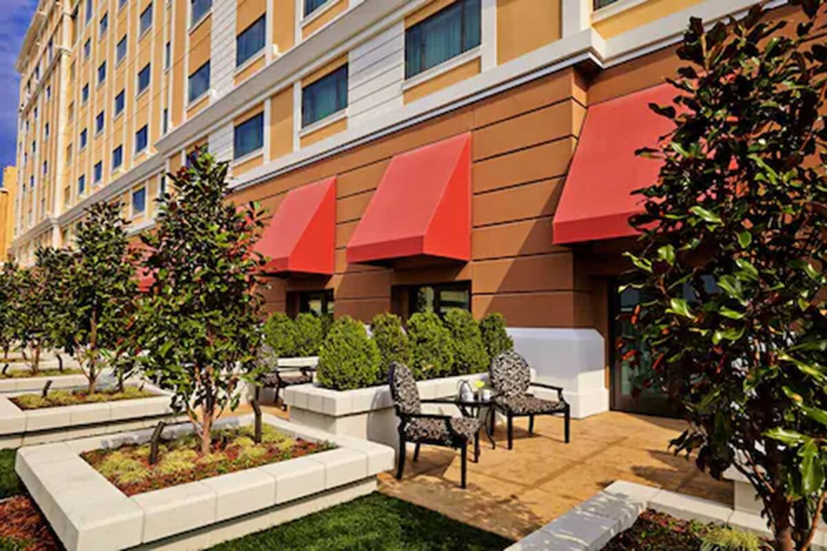 A hotel with a modern facade, outdoor seating area with chairs and tables, and a well-maintained garden.