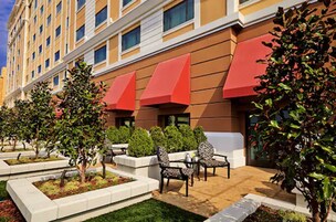 Un hotel con una facciata moderna, un'area esterna con sedute e tavoli, e un giardino curato.