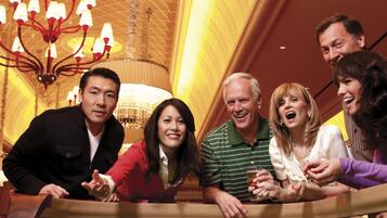 A group of people at a craps table in a casino with a chandelier and a high ceiling.
