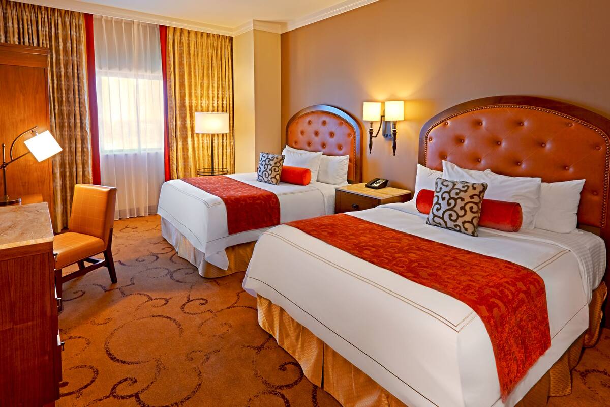 A hotel room with two beds, a desk, and a chair.