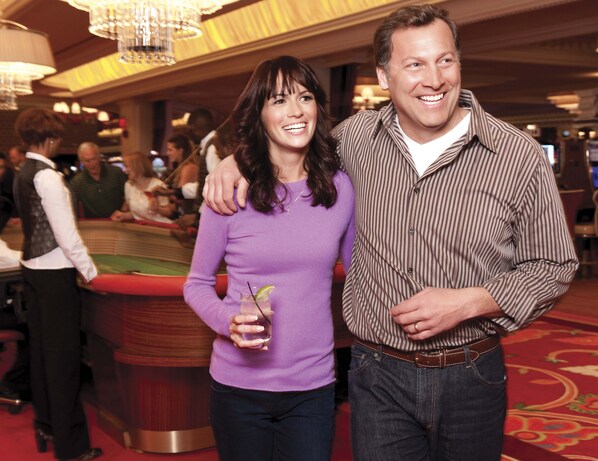 A man and a woman standing in a hotel lobby with a pool table and other guests in the background.