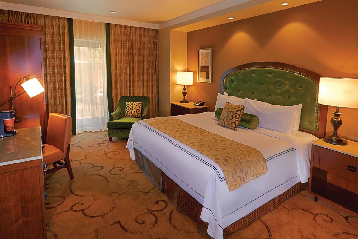A hotel room with a bed, a desk, a chair, a nightstand, and a lamp.