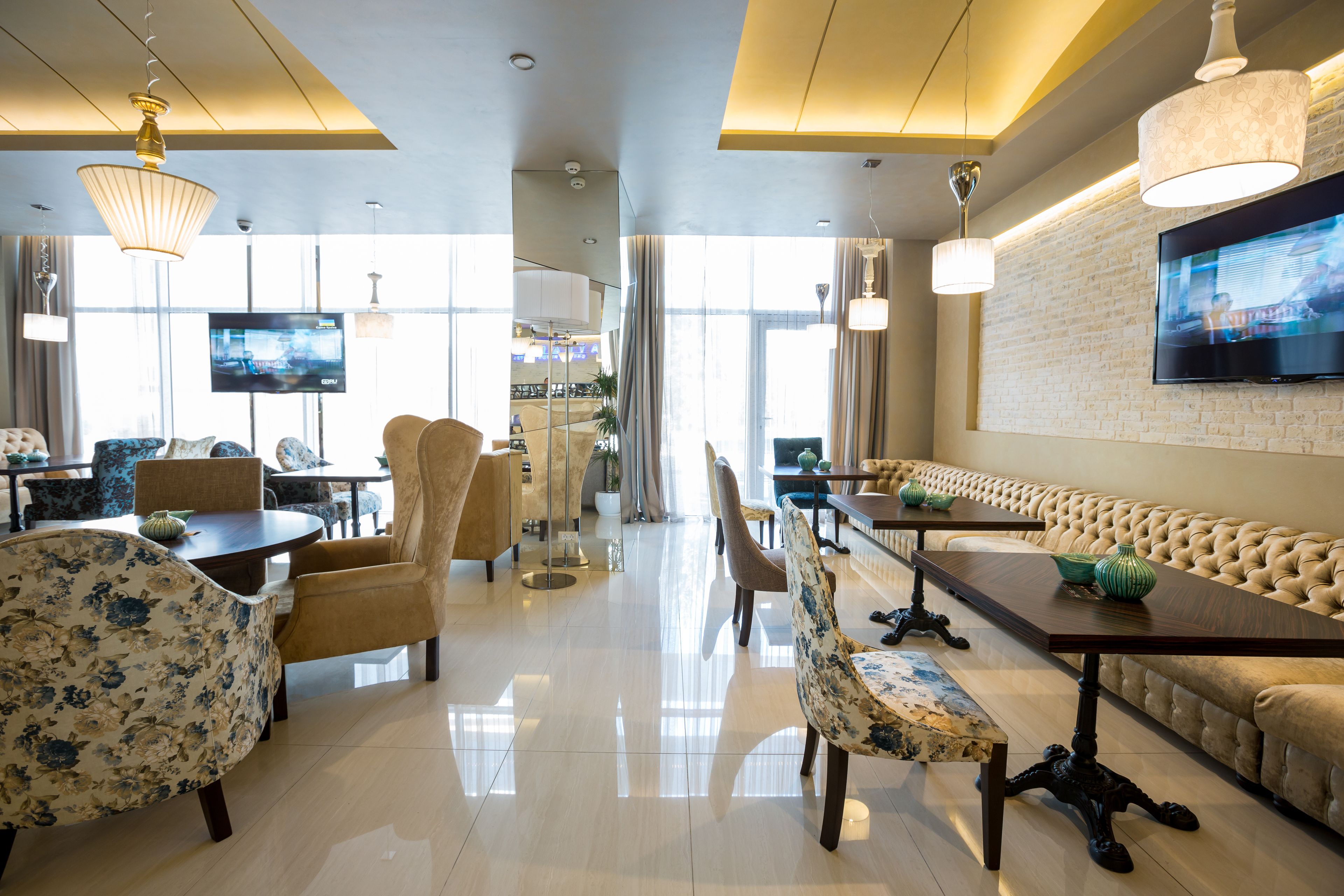 Een ruime hotel lobby met een centraal gelegen zitgedeelte, een aan de muur bevestigde televisie en een moderne kroonluchter.