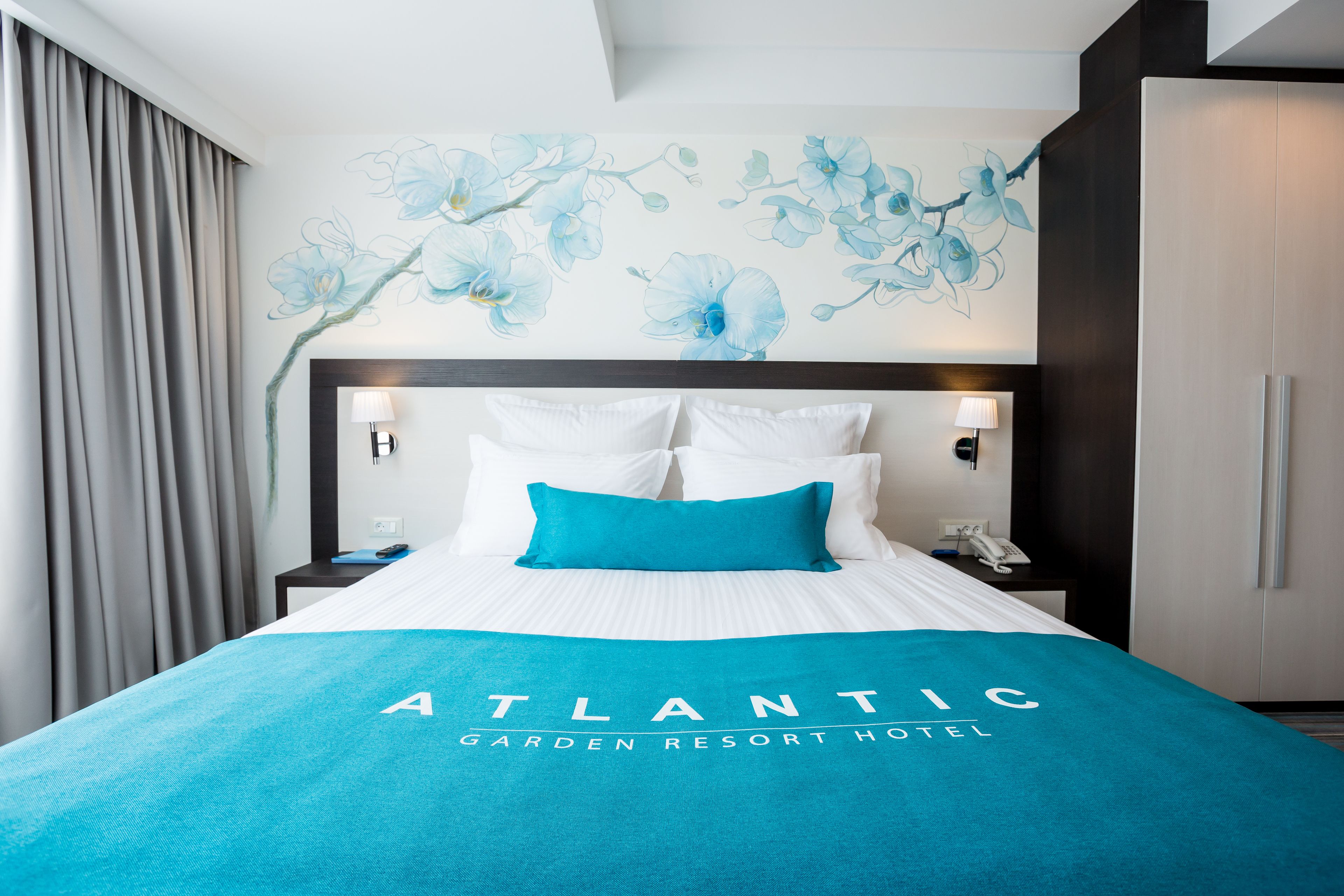 Hotelkamer met een bed, nachtkastje, lamp, telefoon en een muur met een bloemmotief.