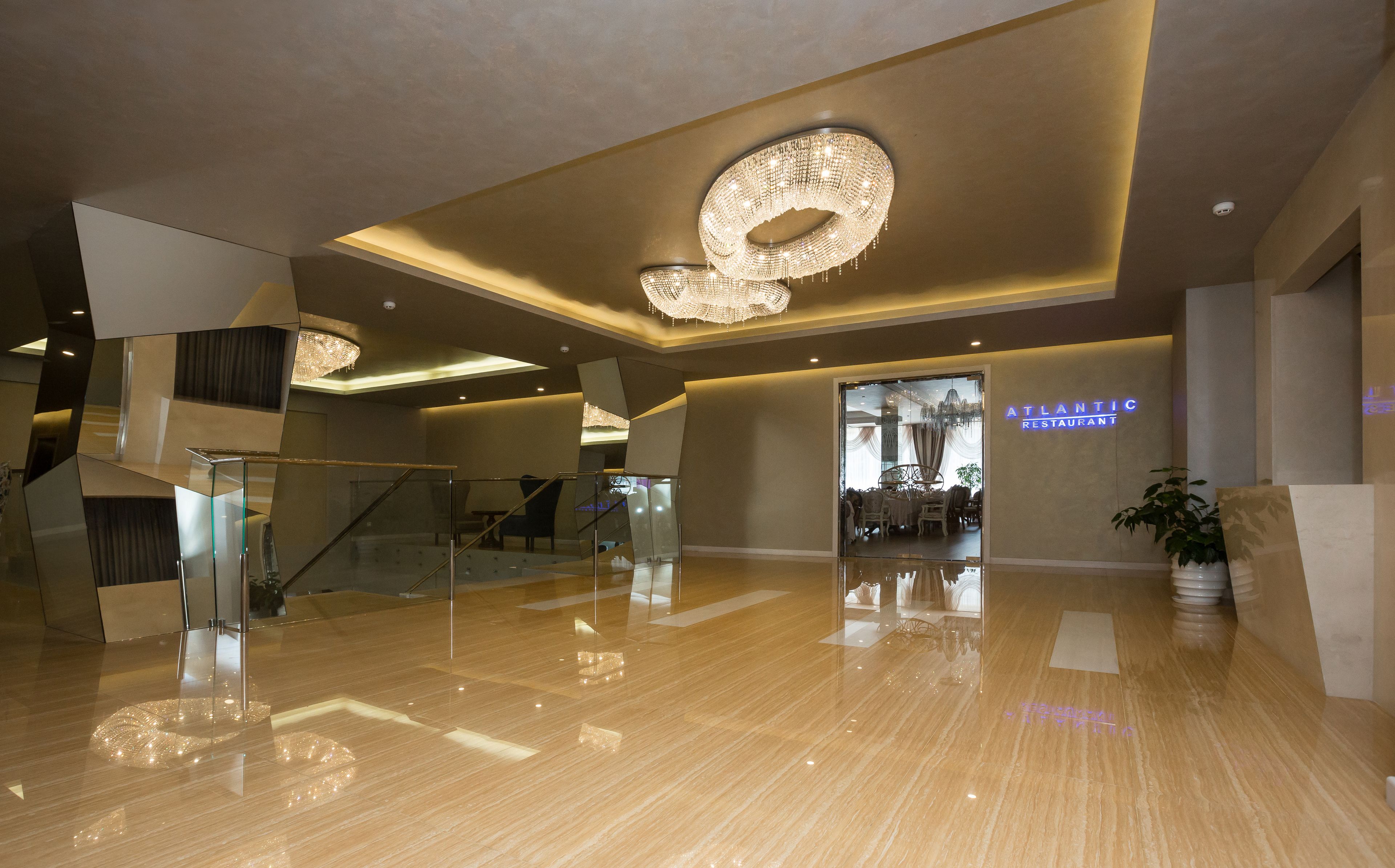 A modern lobby with a polished marble floor, a grand chandelier, and a staircase leading to an upper level.