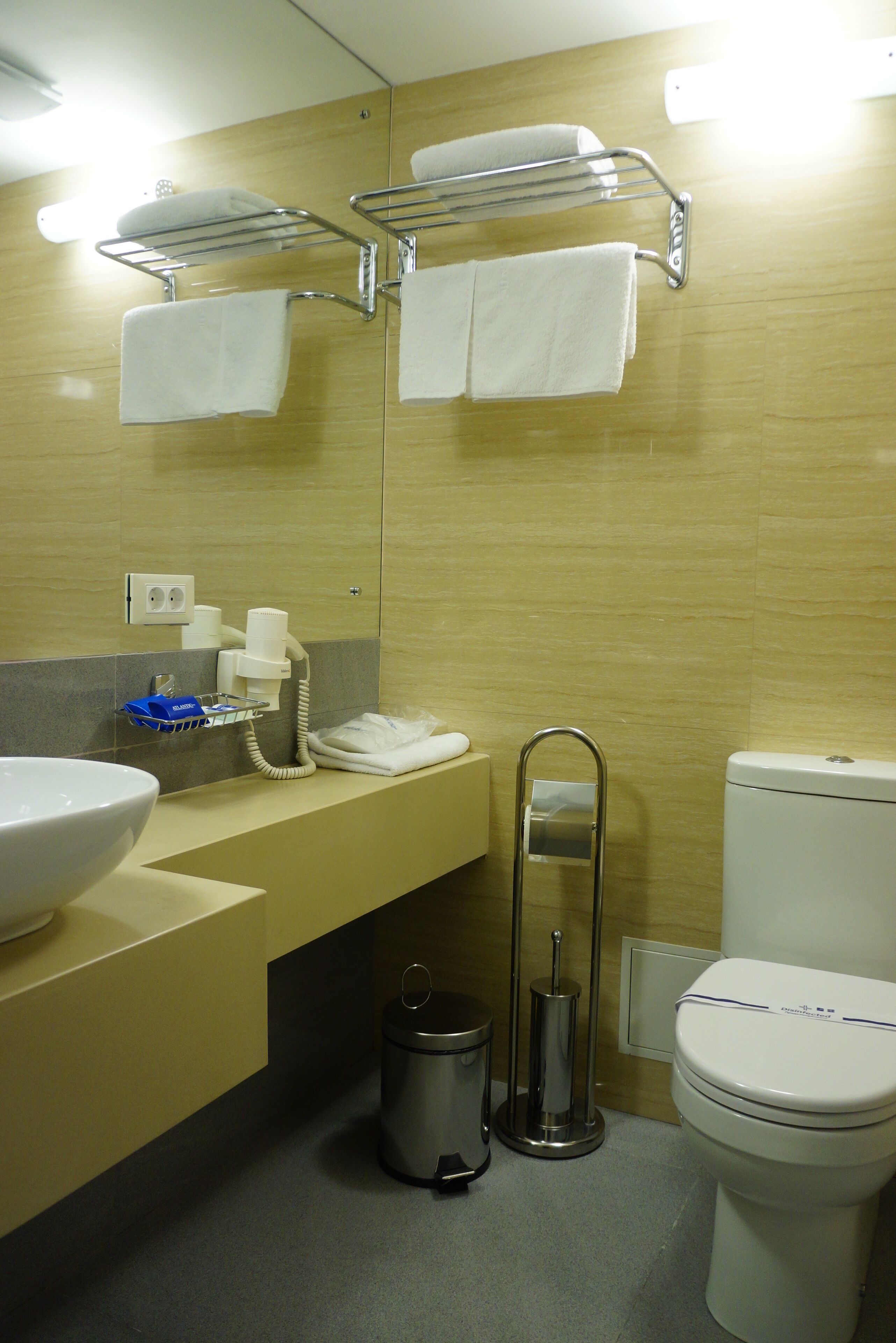 Un baño con lavabo, espejo, toallero, inodoro y cubo de basura.