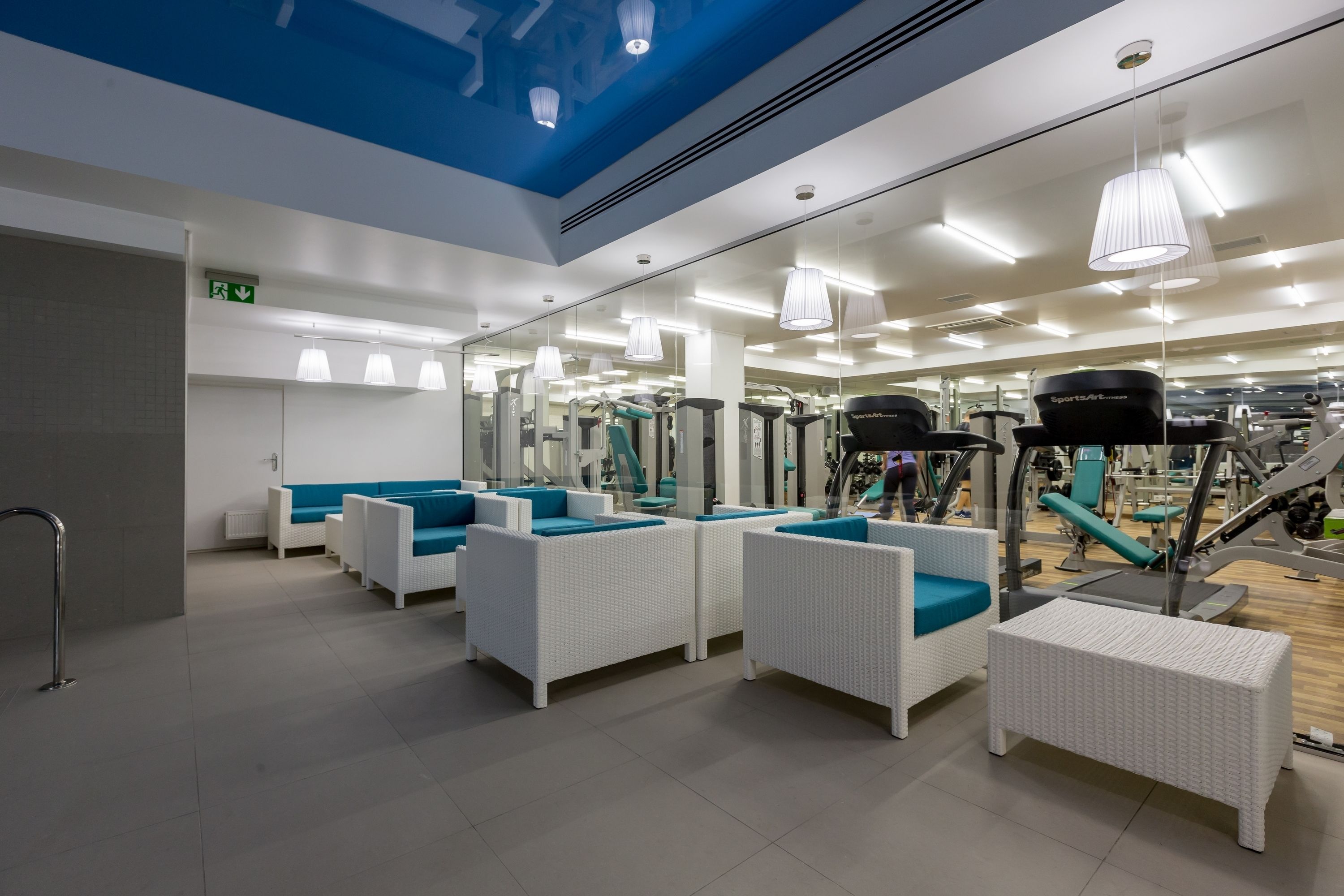 Un gimnasio moderno con mobiliario de mimbre blanco, equipo de ejercicio y techo azul.