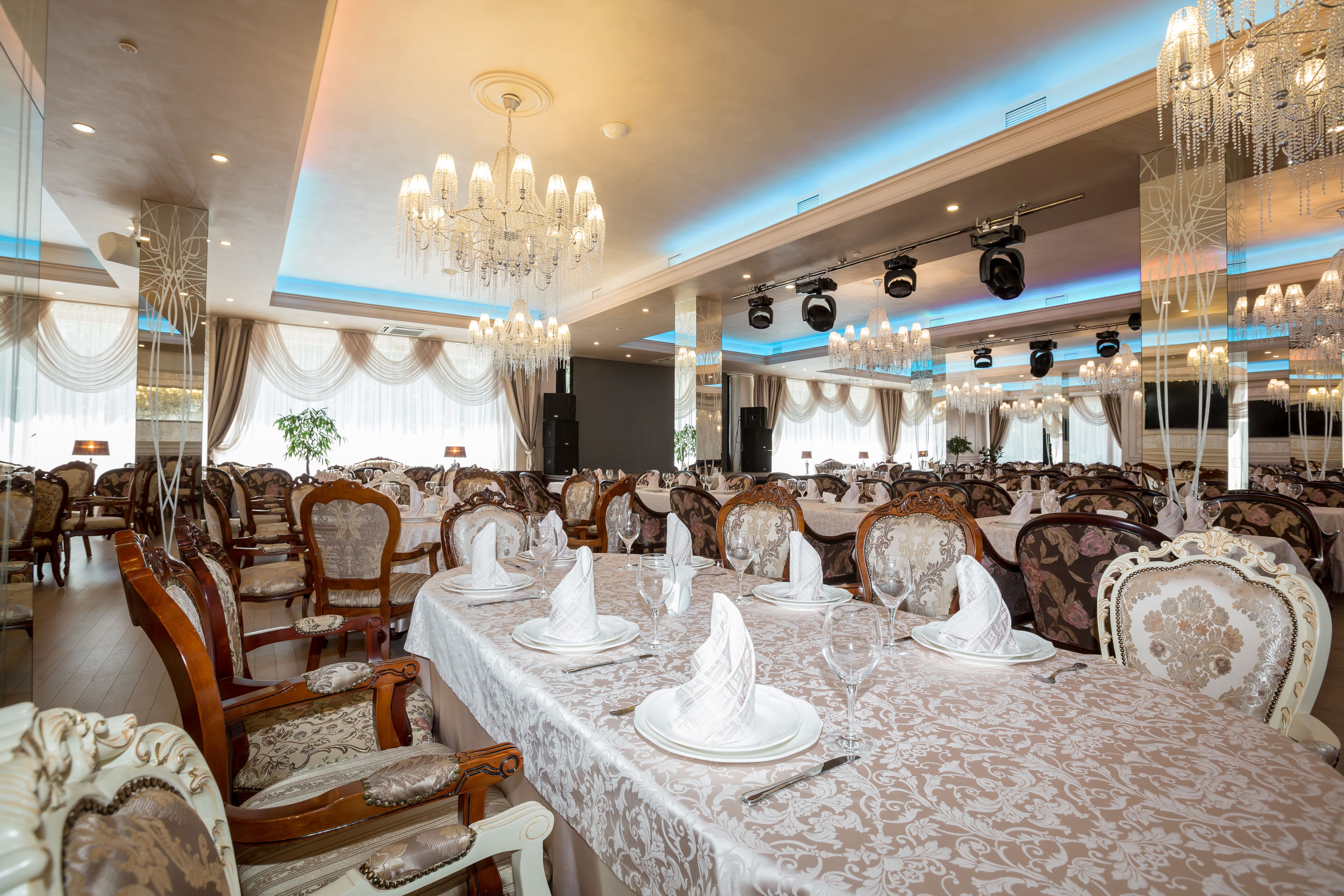 Une salle de banquet agrémentée de lustres somptueux, de tables élégamment dressées et de chaises classiques en bois.