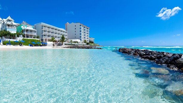 Een strandhotel met meerdere gebouwen, helder turquoise water en een rotsachtige kustlijn.