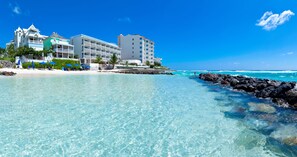A beachfront hotel with multiple buildings, clear turquoise water, and a rocky shoreline.