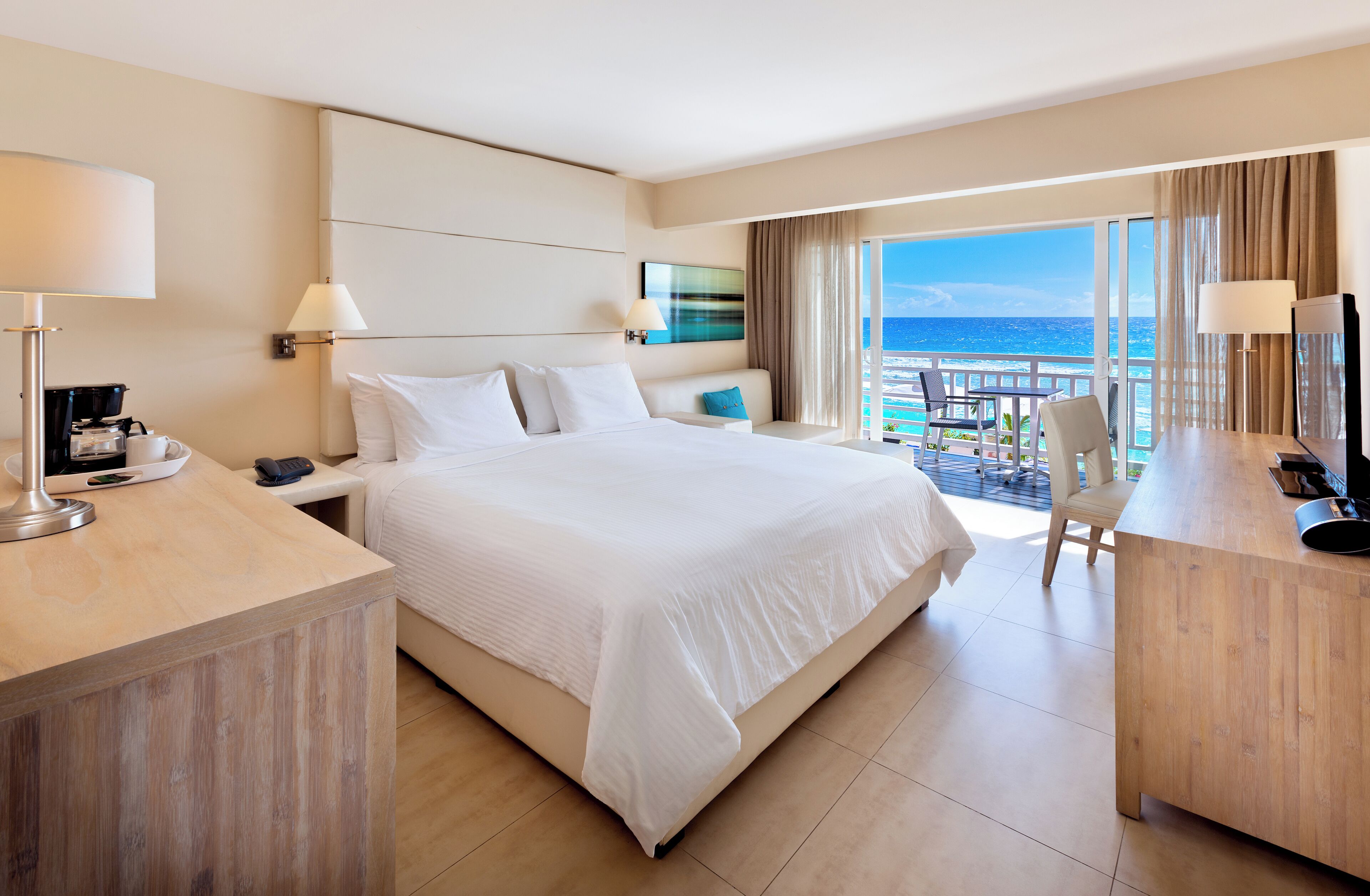 A hotel room with a large bed, a desk, a chair, and a balcony with a view of the ocean.
