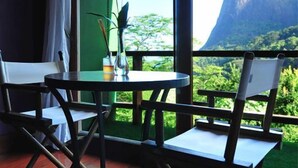 A wooden table with chairs, a vase with flowers, and a view of a mountain through large windows. - TuAkAzA Exclusive Boutique Lodge (Rio de Janeiro)