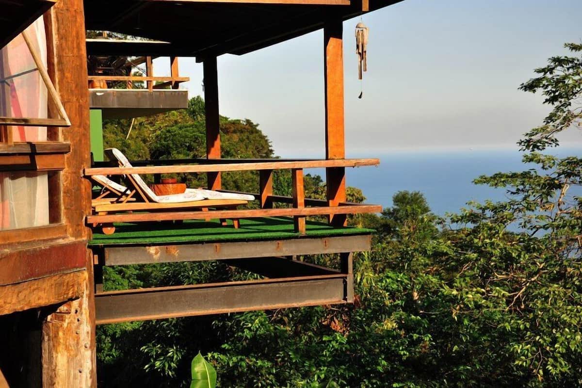 A wooden structure with a balcony and lounge chairs overlooking a body of water.