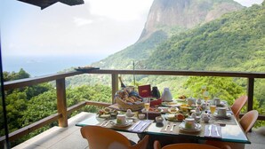 A dining table set with plates, utensils, and a variety of food items, overlooking a lush green landscape and a prominent mountain. - TuAkAzA Exclusive Boutique Lodge (Rio de Janeiro)