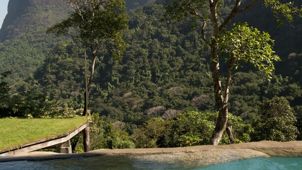 A tranquil outdoor setting with a clear pool, a metal bucket with a bottle, and two glasses on a rock. - TuAkAzA Exclusive Boutique Lodge (Rio de Janeiro)