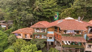 A traditional wooden house with a tiled roof, surrounded by lush greenery and a Brazilian flag. - TuAkAzA Exclusive Boutique Lodge (Rio de Janeiro)