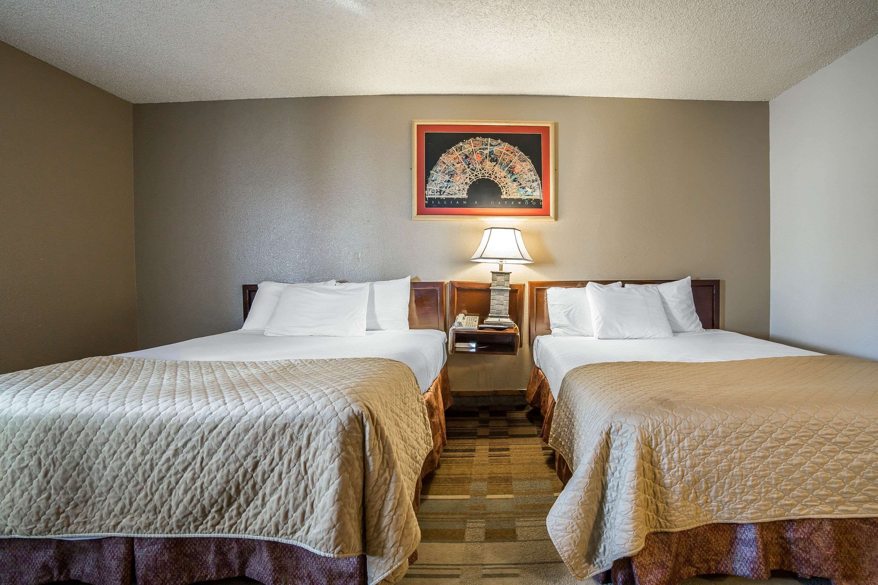 A hotel room with two beds, a nightstand with a lamp, and a framed picture on the wall.