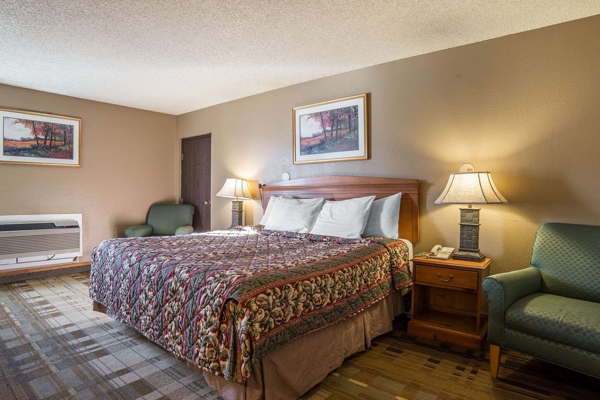 A hotel room with a large bed, two bedside tables with lamps, a chair, and two framed pictures on the walls.
