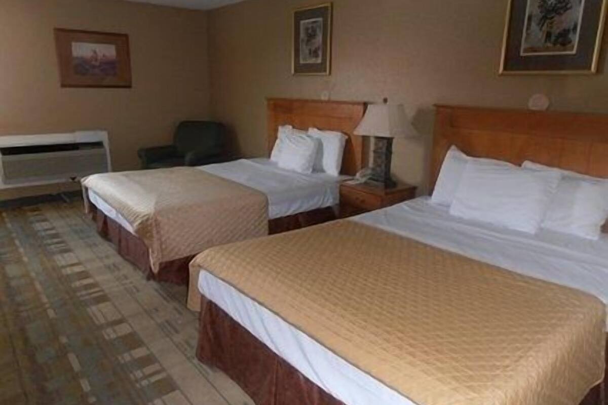 Una habitación de hotel con dos camas, una silla, un escritorio y una lámpara.