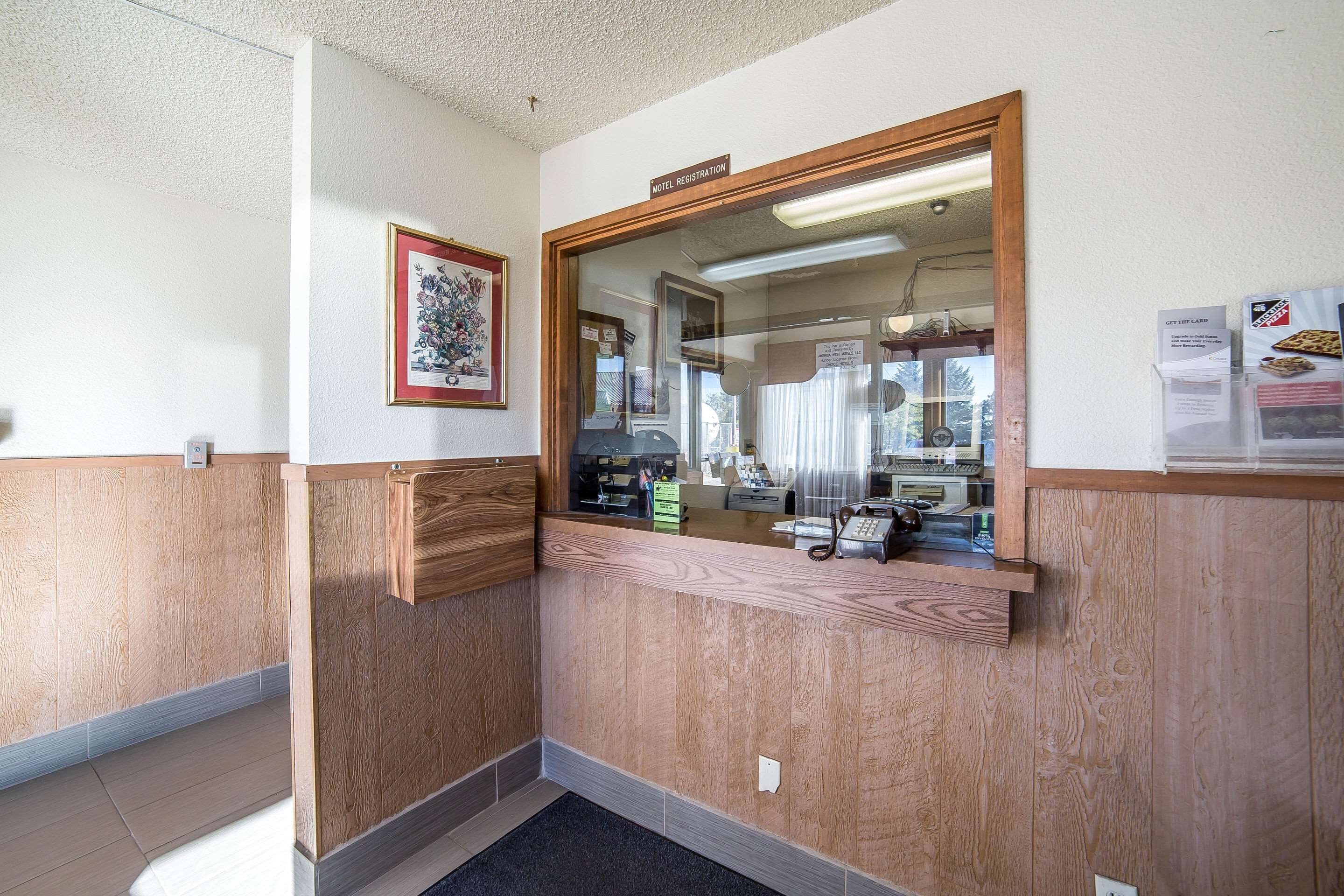 Ein Hotel-Empfangsbereich mit einem hölzernen Empfangstresen, einem gerahmten Bild an der Wand und einem Schild über dem Tresen mit der Aufschrift 'Motel Registration'.