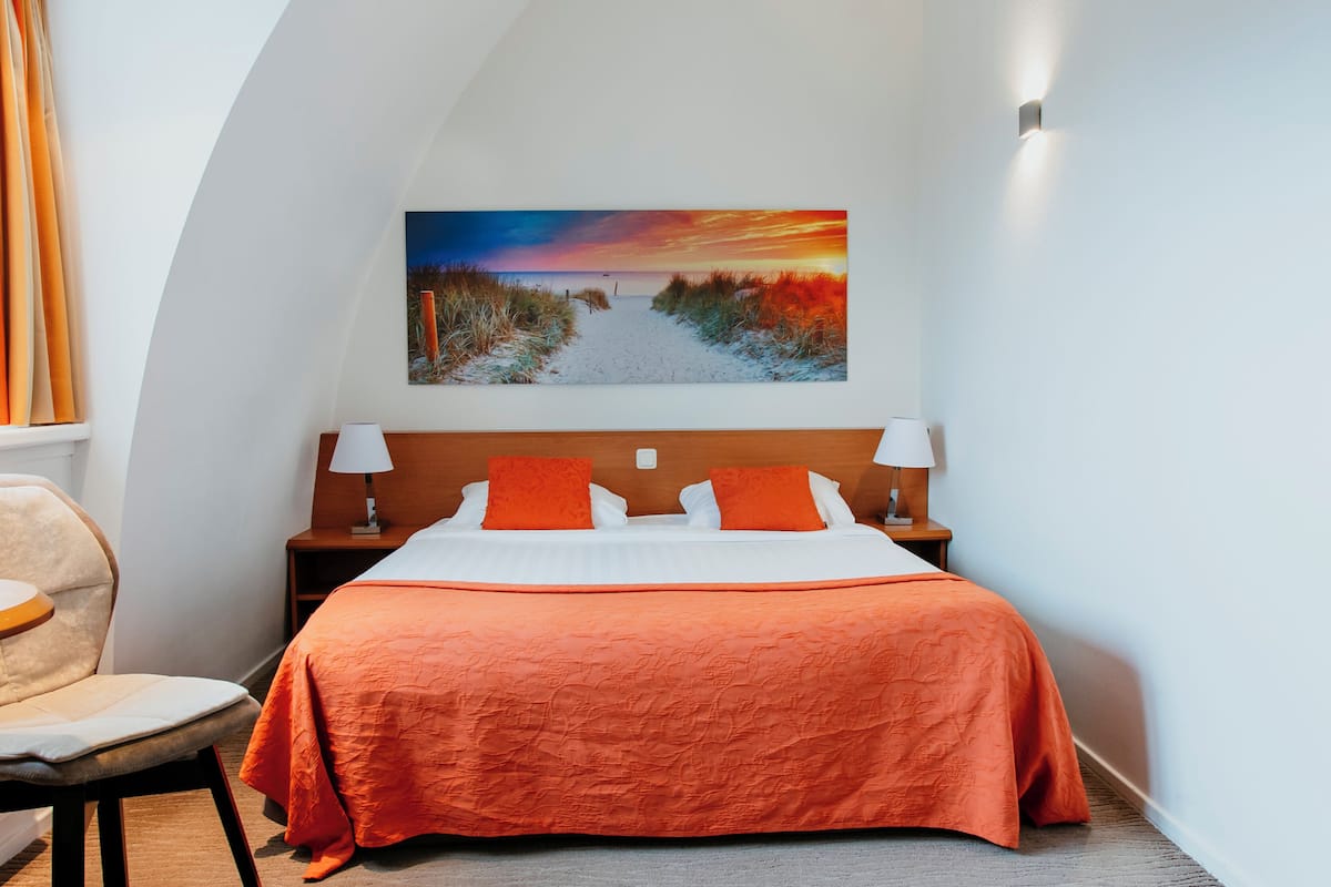 A hotel room with a large bed, two nightstands, a chair, and a painting of a sunset over a beach.