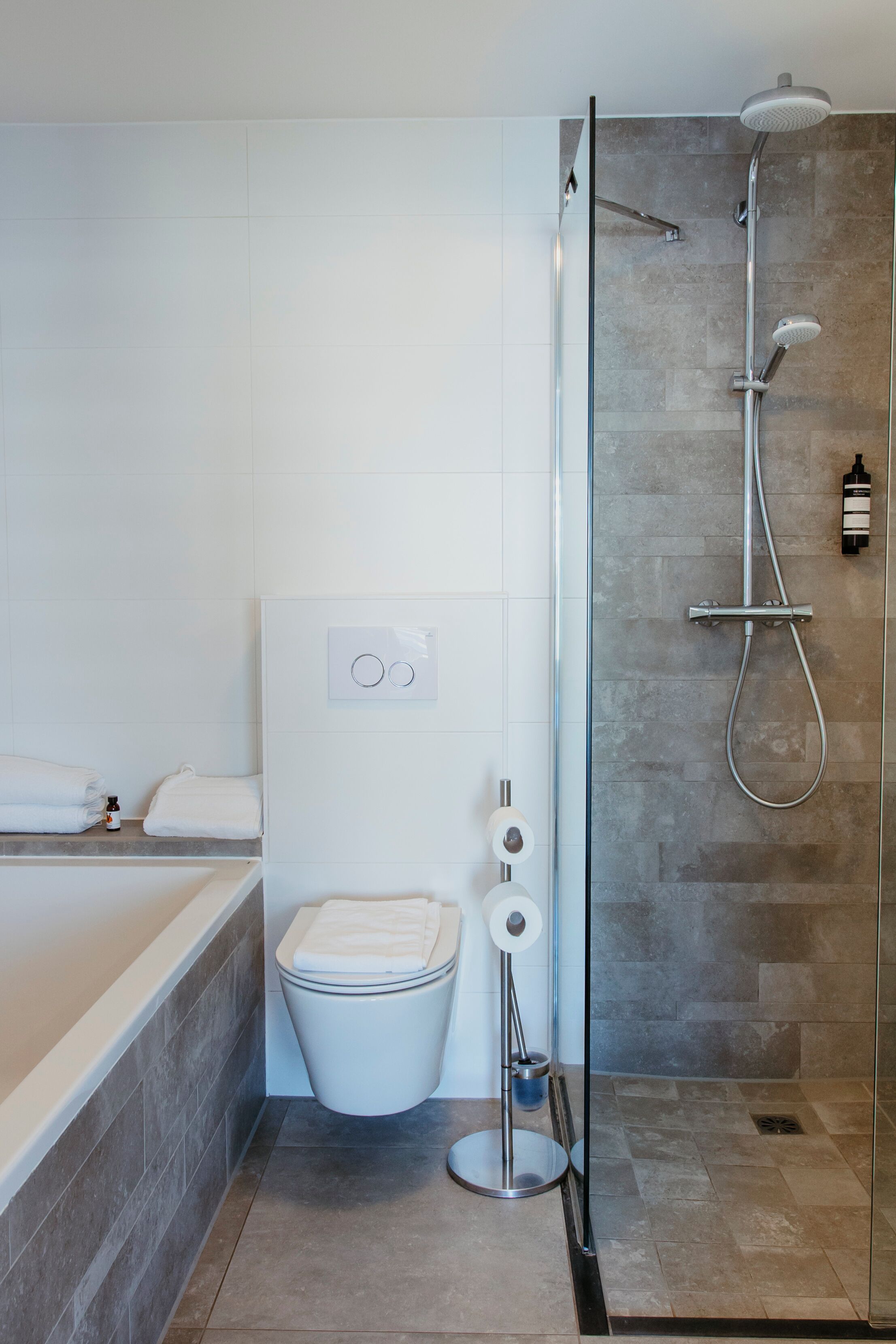 Een moderne badkamer met een douche met glazen wand, een wit toilet en een bad.