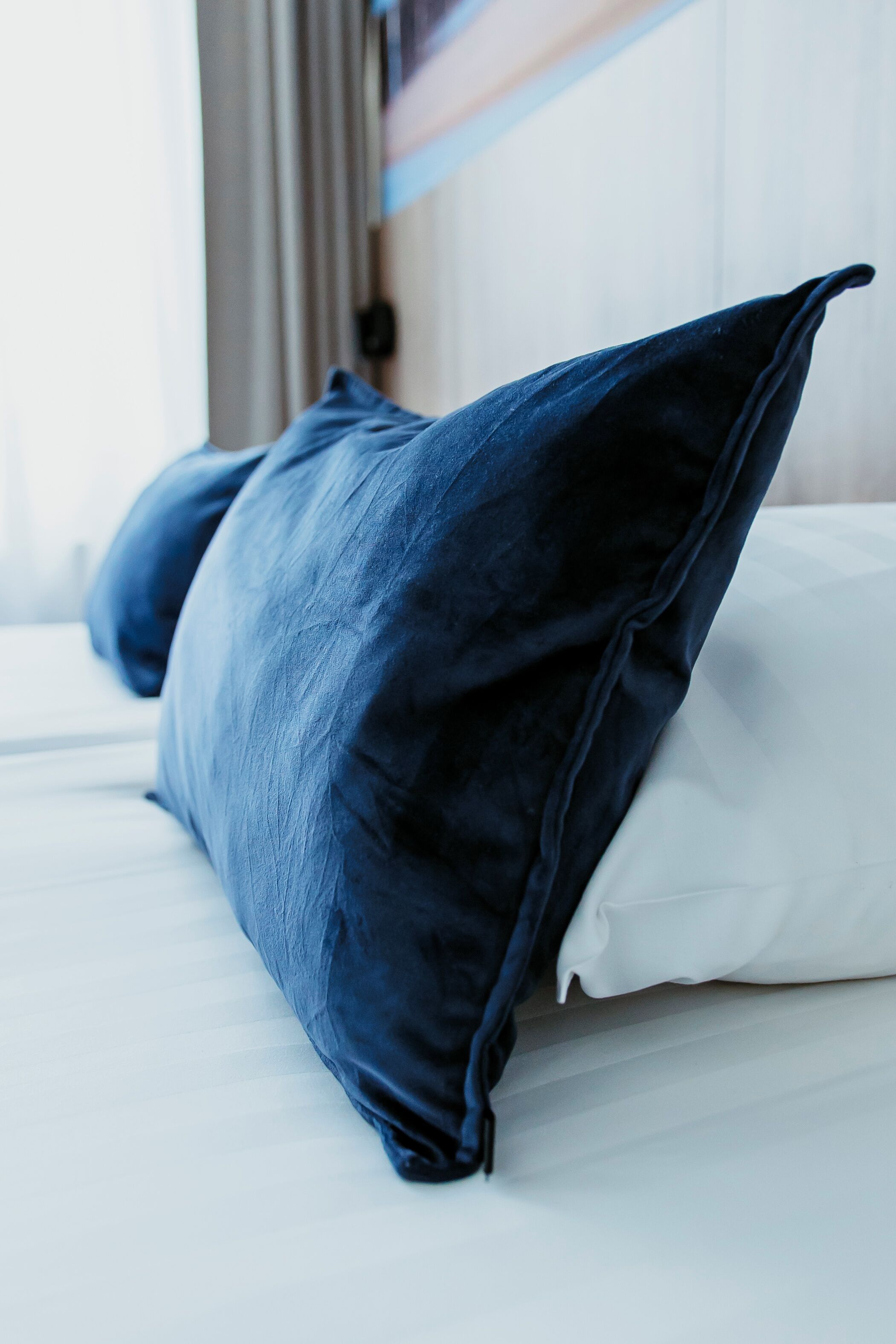 A bed with two pillows, one dark blue and one white, in a hotel room.