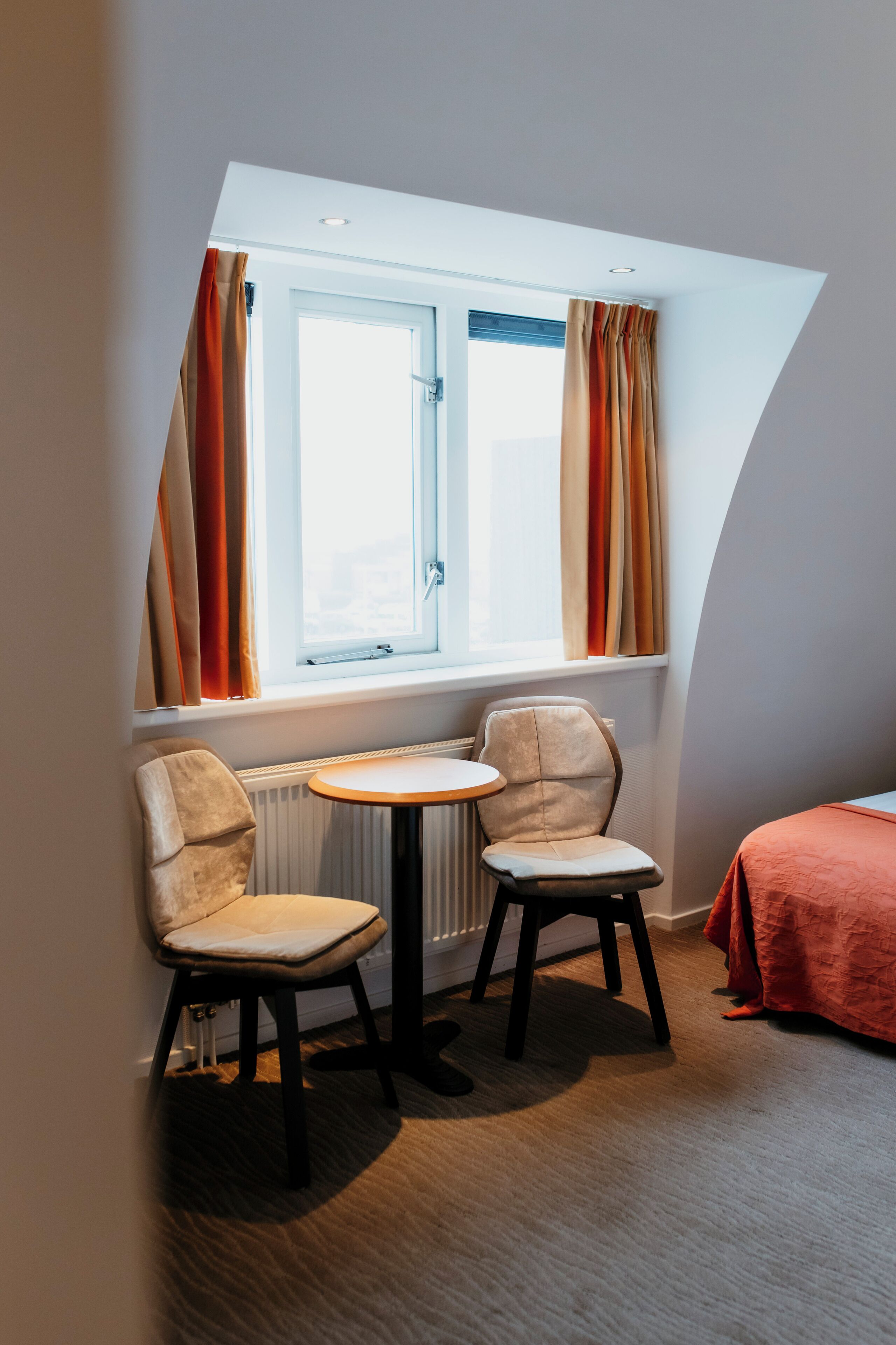 A corner room with a window, two chairs, a small table, and a radiator.
