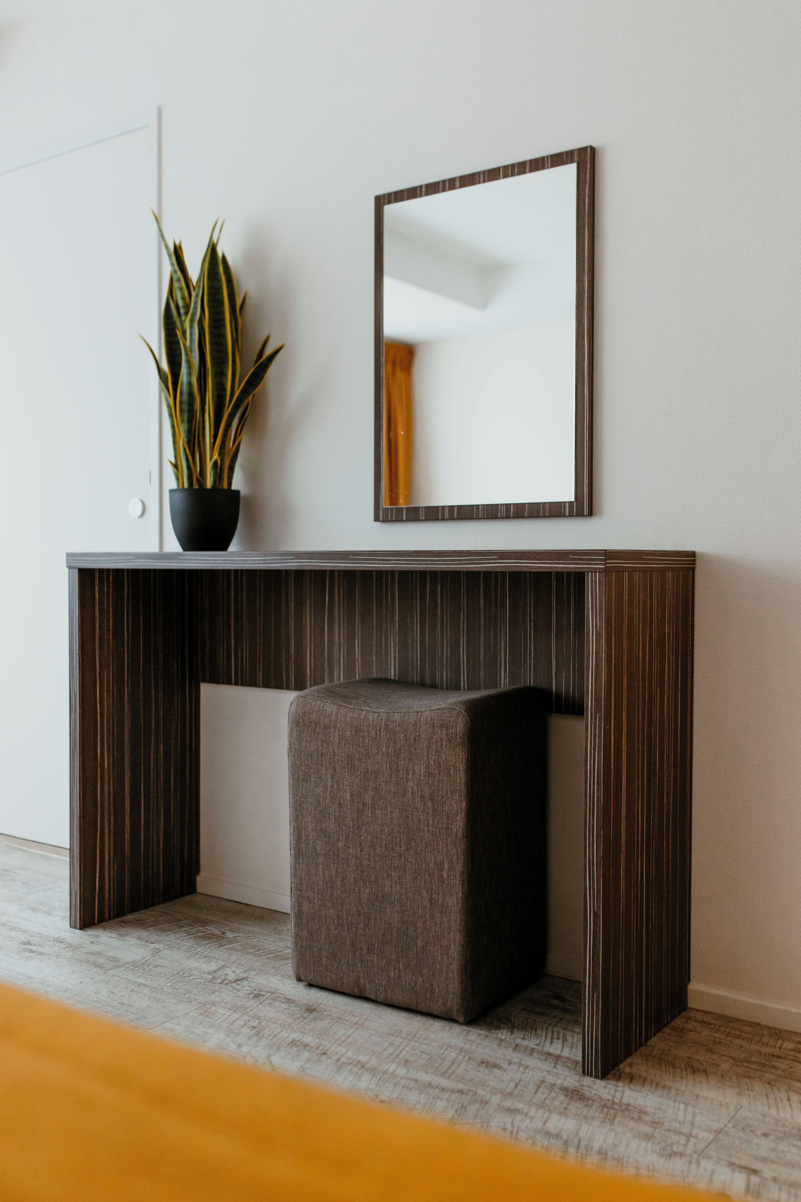 A modern desk with a dark wood finish, a small potted plant, and a mirror.